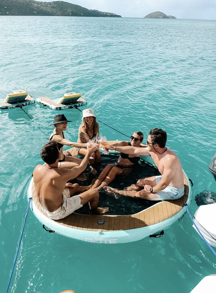 Guests with drinks on a floating platform beside the yacht