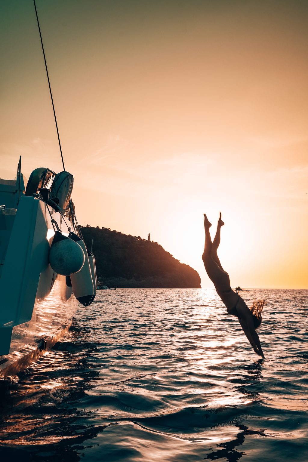 A guest jumping from a catamaran into the sea at sunset