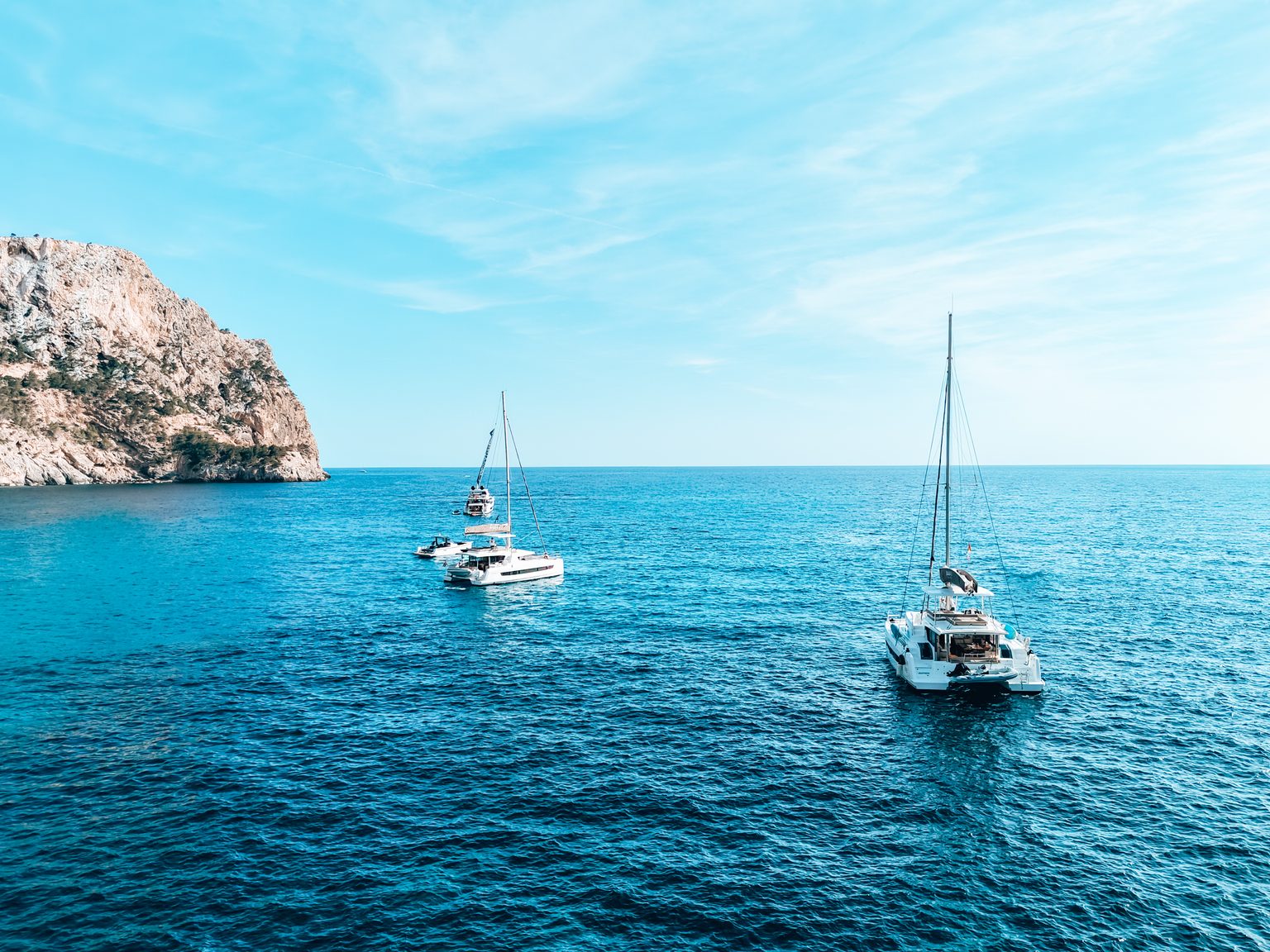 Two catamarans sailing on open water near a headland